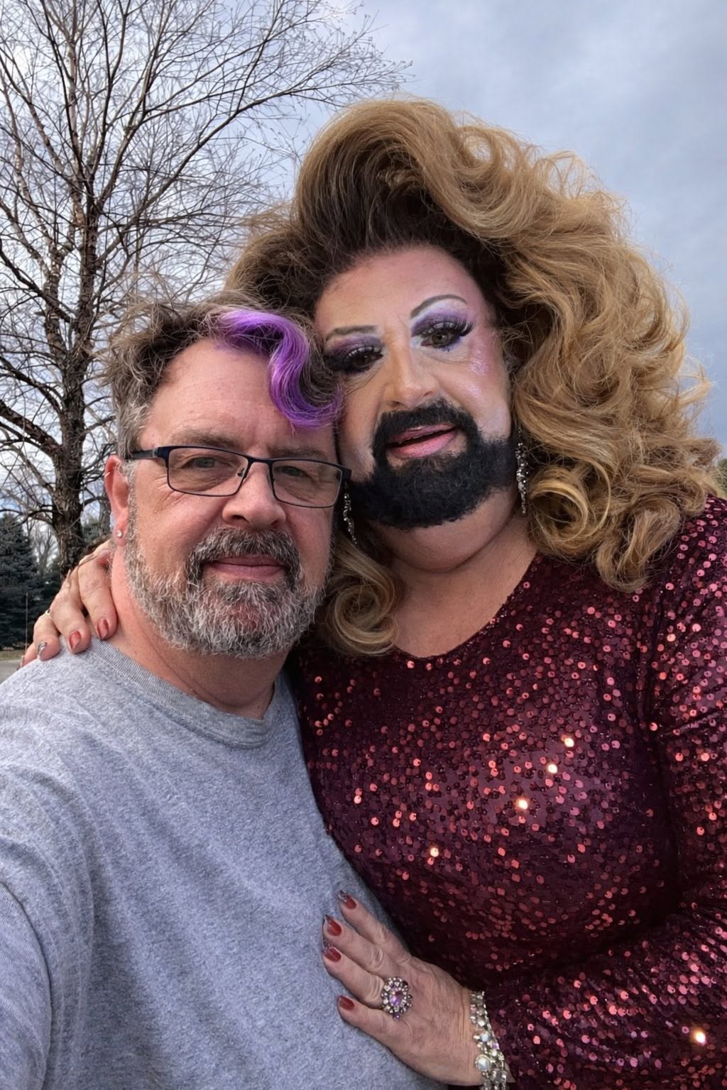 Jim Guerrant out of drag posing outdoors with Jessica St. James in burgundy sequins