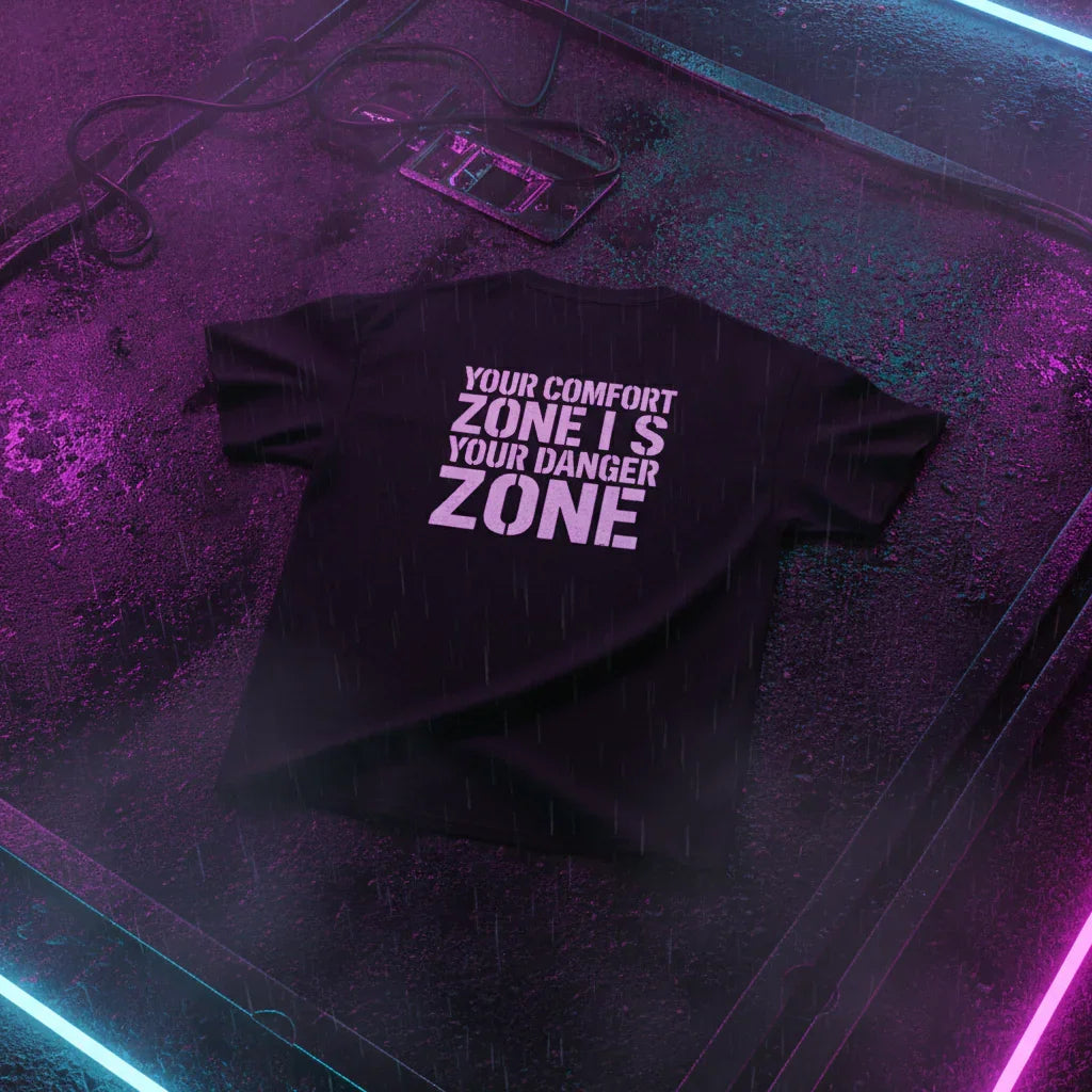 Black motivational graphic tee on wet neon-lit street, text 'Your comfort zone is your danger zone'