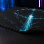 Macro view of the UFO mouse pad showing the cyan artwork, woven fabric, stitched edge and non-slip rubber base.

