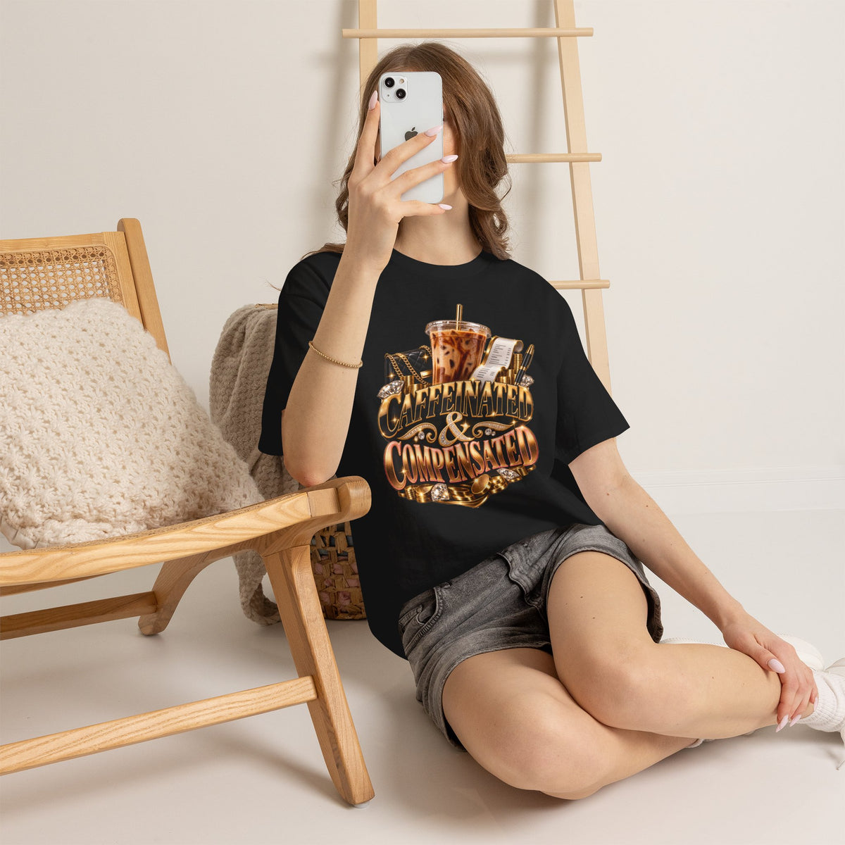 Woman wearing the Caffeinated & Compensated black graphic tee in a casual coffee-inspired setting