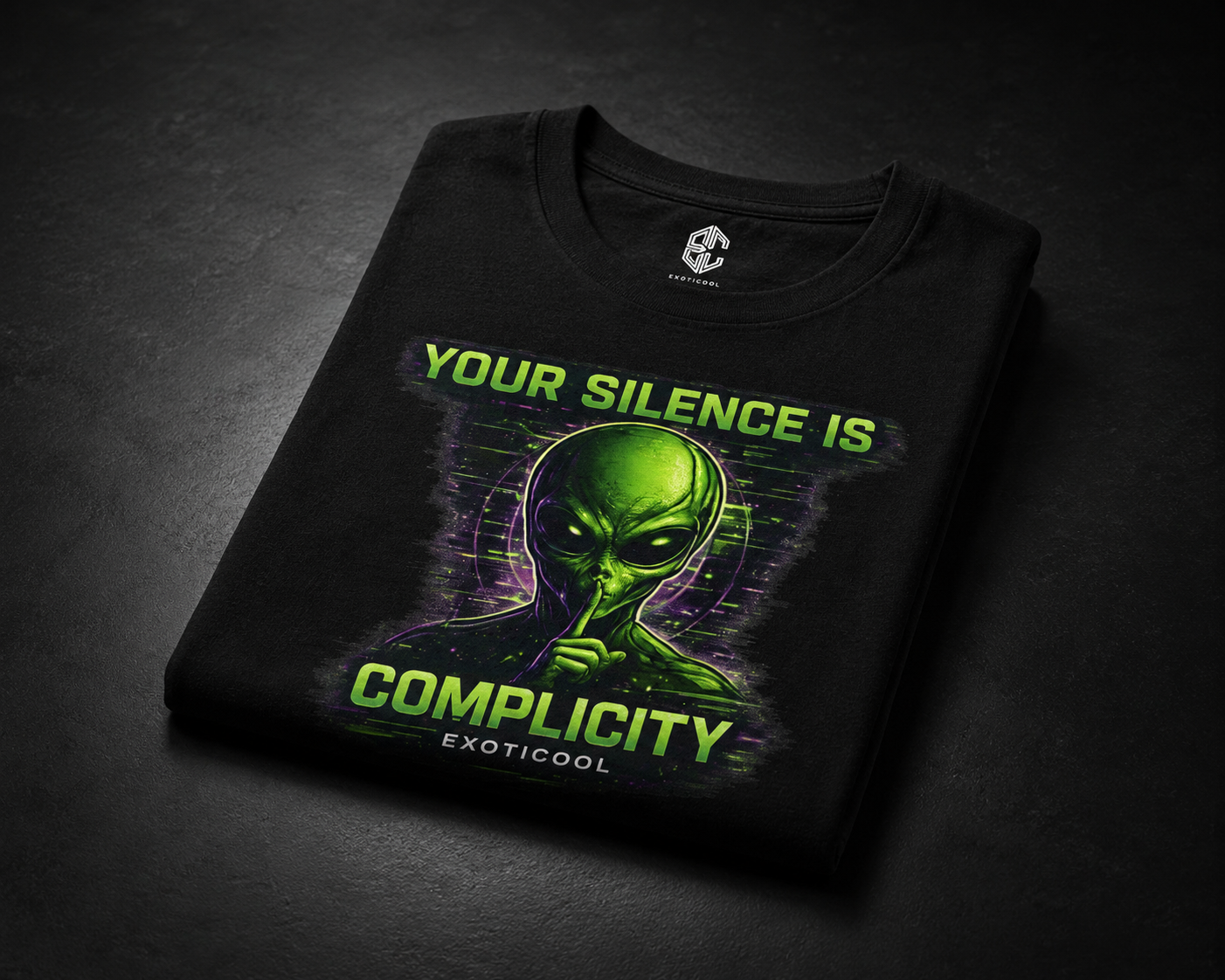 Folded Exoticool Your Silence Is Complicity black alien graphic T-shirt displayed on a matte black surface, showcasing the premium DTG print, cotton fabric, and printed inner neck label.