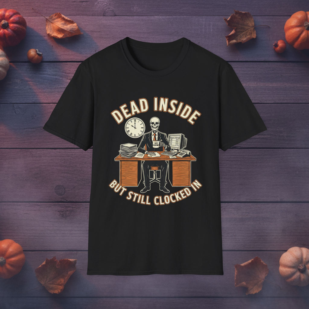 A black short-sleeve graphic t-shirt displayed flat on a dark purple wooden background decorated with autumn leaves and small pumpkins. The graphic features a skeleton in a suit sitting at a desk with a clock, with the text 'DEAD INSIDE BUT STILL CLOCKED IN' in a beige font.