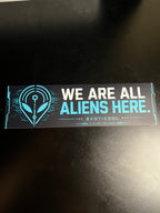 Real 11-inch We Are All Aliens Here bumper sticker displayed flat on a black surface