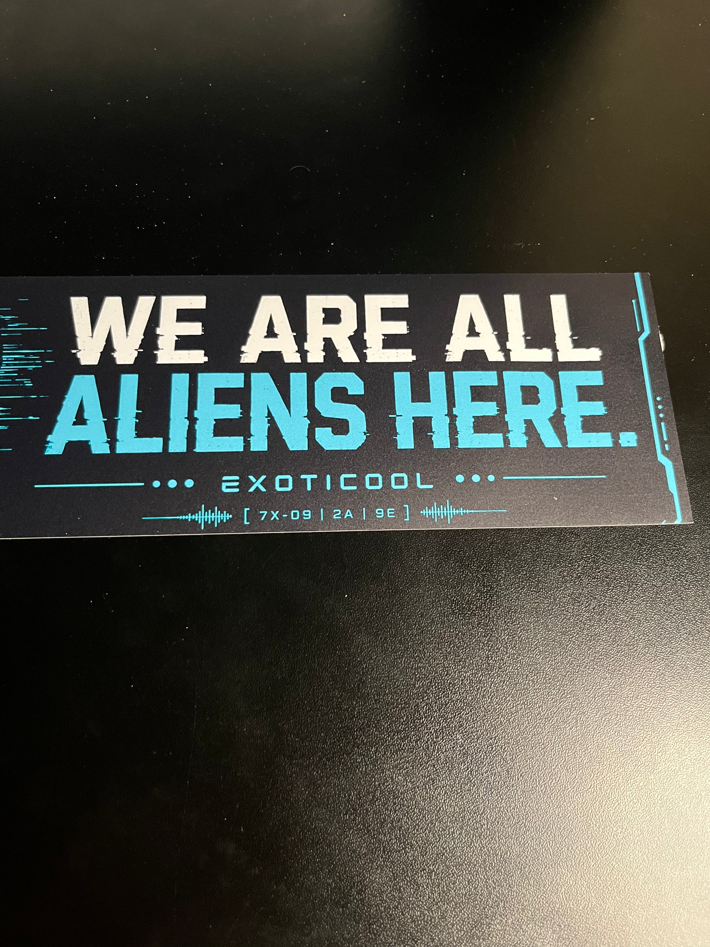 Close-up of the We Are All Aliens Here lettering and Exoticool branding on the bumper sticker