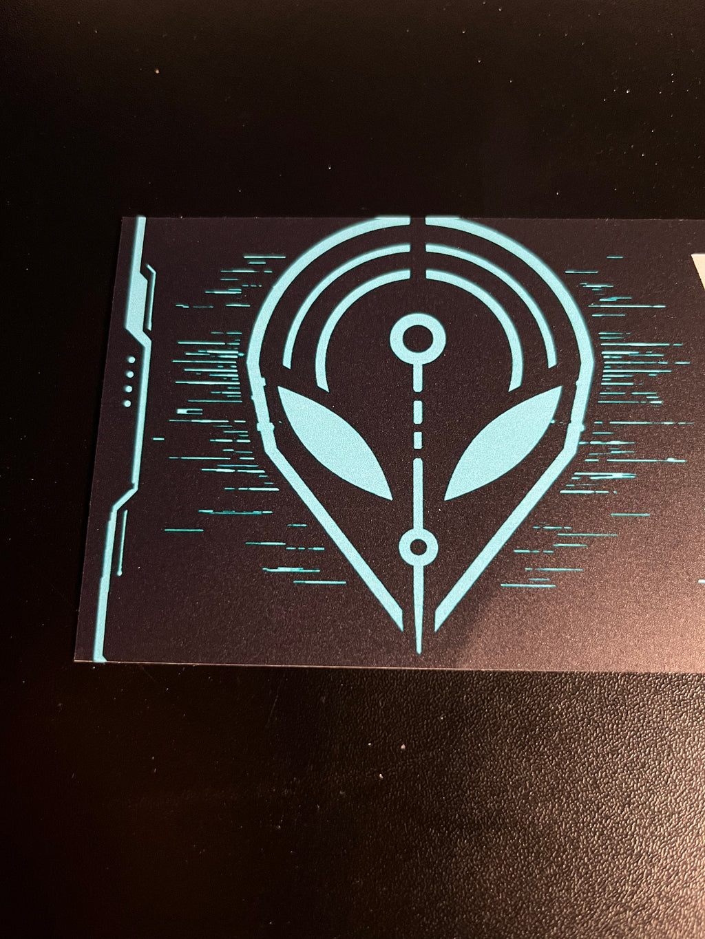 Close-up of the cyan alien signal emblem printed on the black bumper sticker