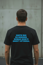 Back view of male model wearing black Exoticool Earth Has No Borders Tee featuring “Earth Has No Borders. Human Rights Aren’t Optional.” statement graphic in an urban setting
