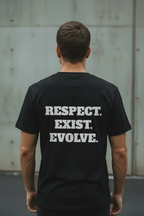 Back view of male model wearing black Exoticool Transphobes Are Trash Tee featuring “Respect. Exist. Evolve.” statement graphic in an urban setting